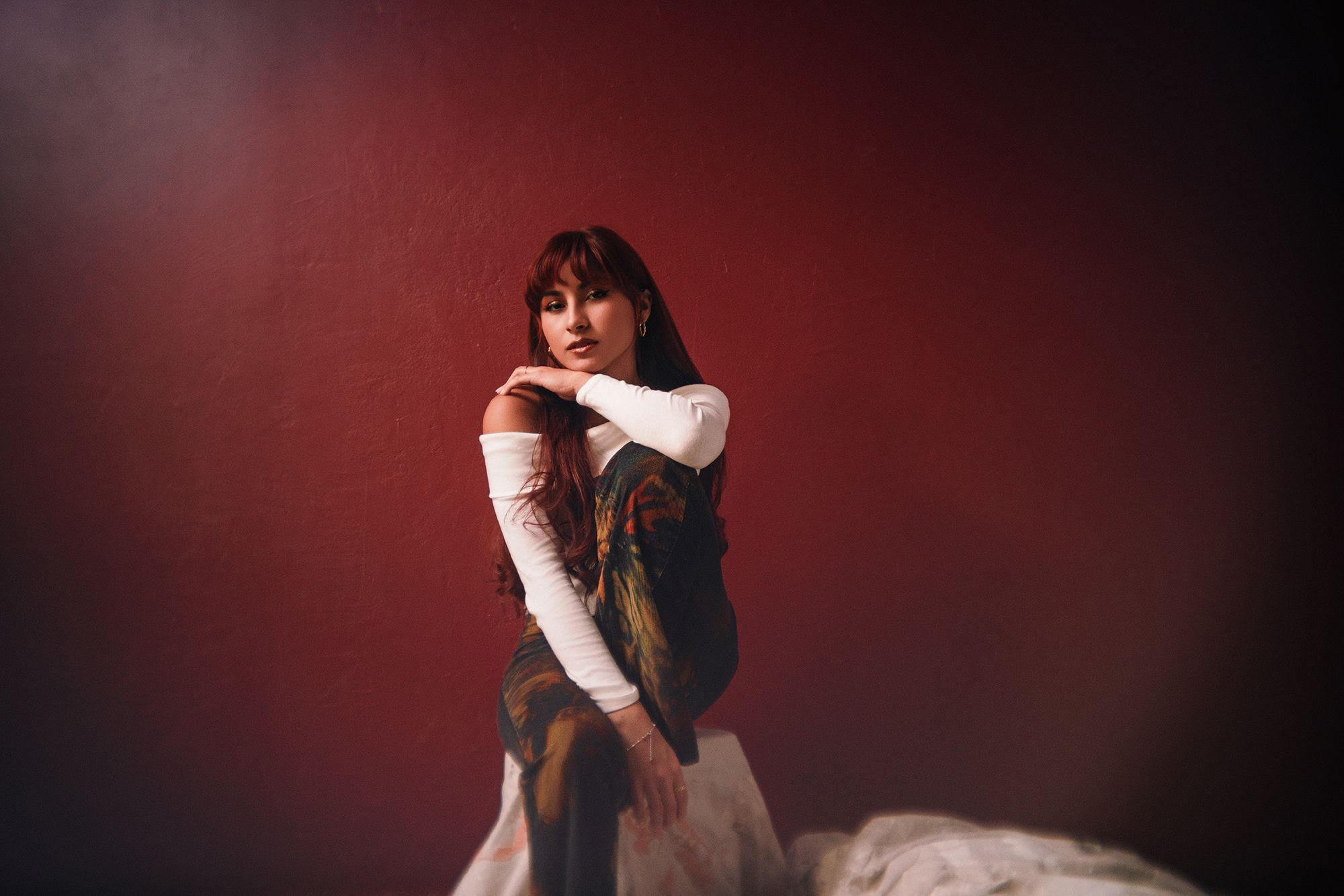 Angel Cintron sitting in front of a maroon backdrop. [Credit: Josh Huskin]